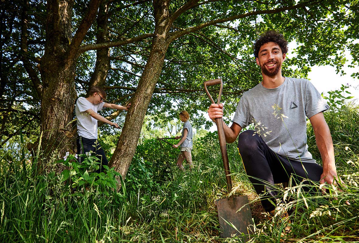 Three young people in a wooded area, about to undertake woodland conservation