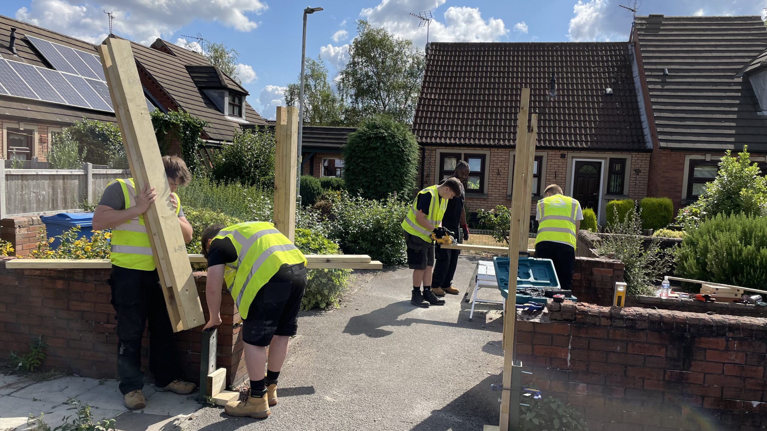 Group of young men wearing yellow high visibility jackets working with wooden planks in residential area.