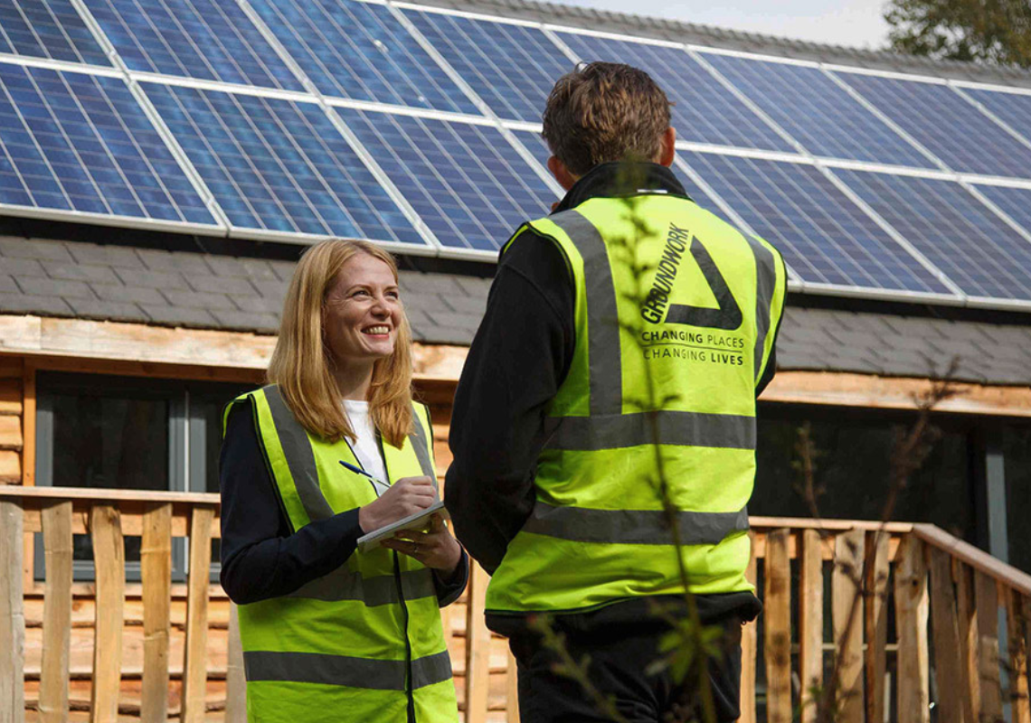 A man and a woman in high visibility jackets stood in front of a building with solar panels