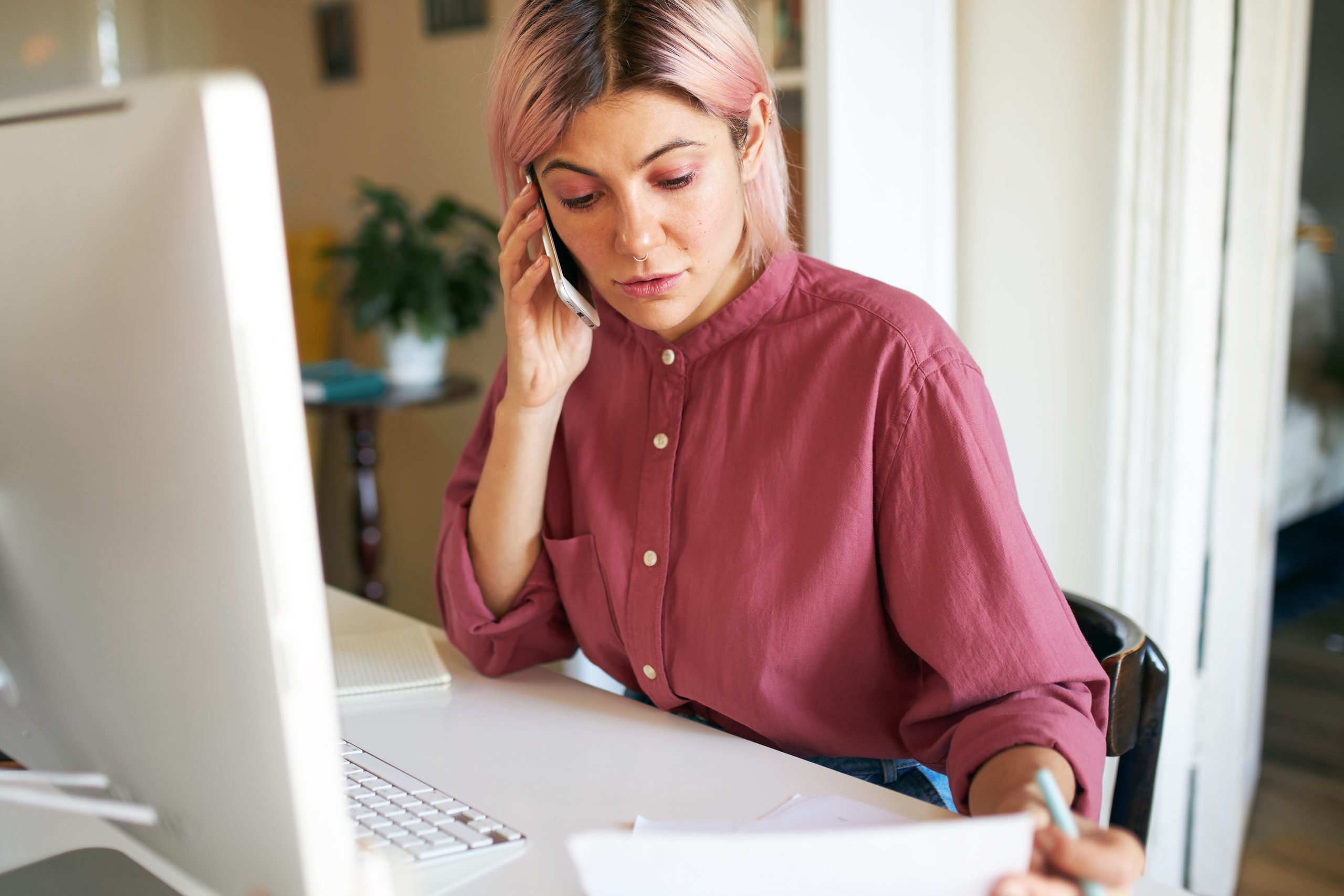 young female with pinkish hair on phone at desk