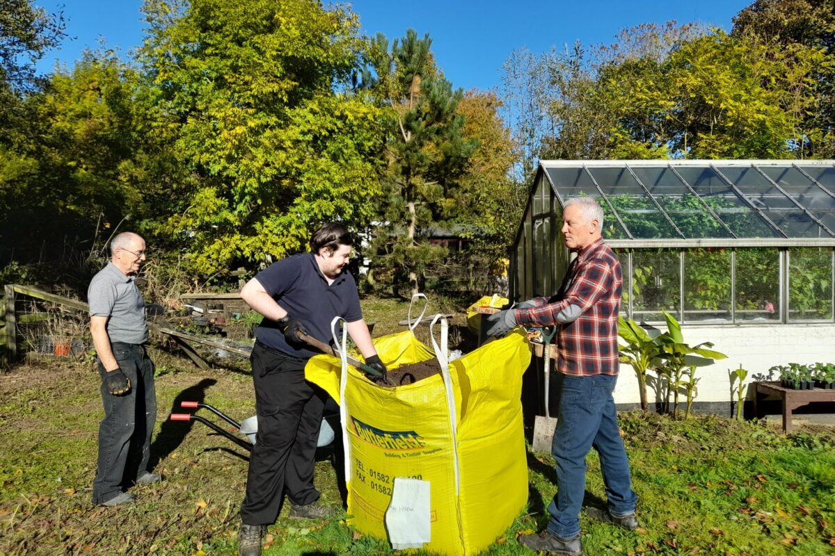 Volunteers filling a compost bag in a garden