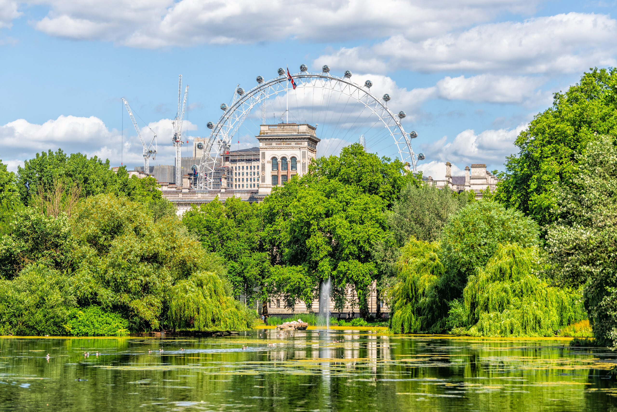 London Eye cityscape view building with St James Park green lake pond on summer day and water fountain in UK