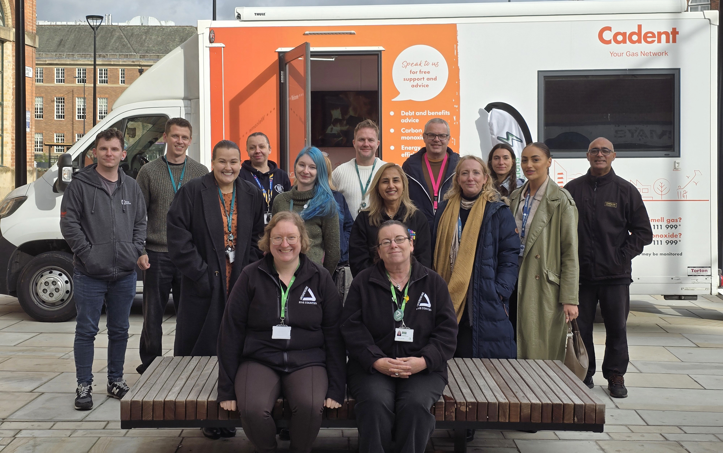 Group of people smiling for the camera in outdoor space with orange and white Cadent branded van in background.