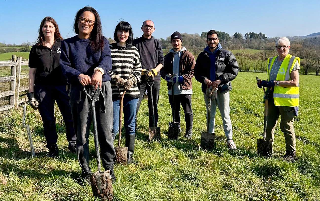 Group of people with shovels standing in field, smiling at camera