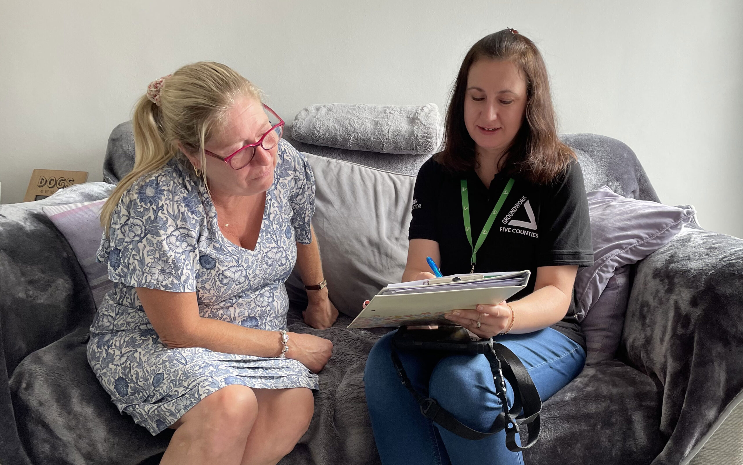 Two women sitting on sofa with paperwork.