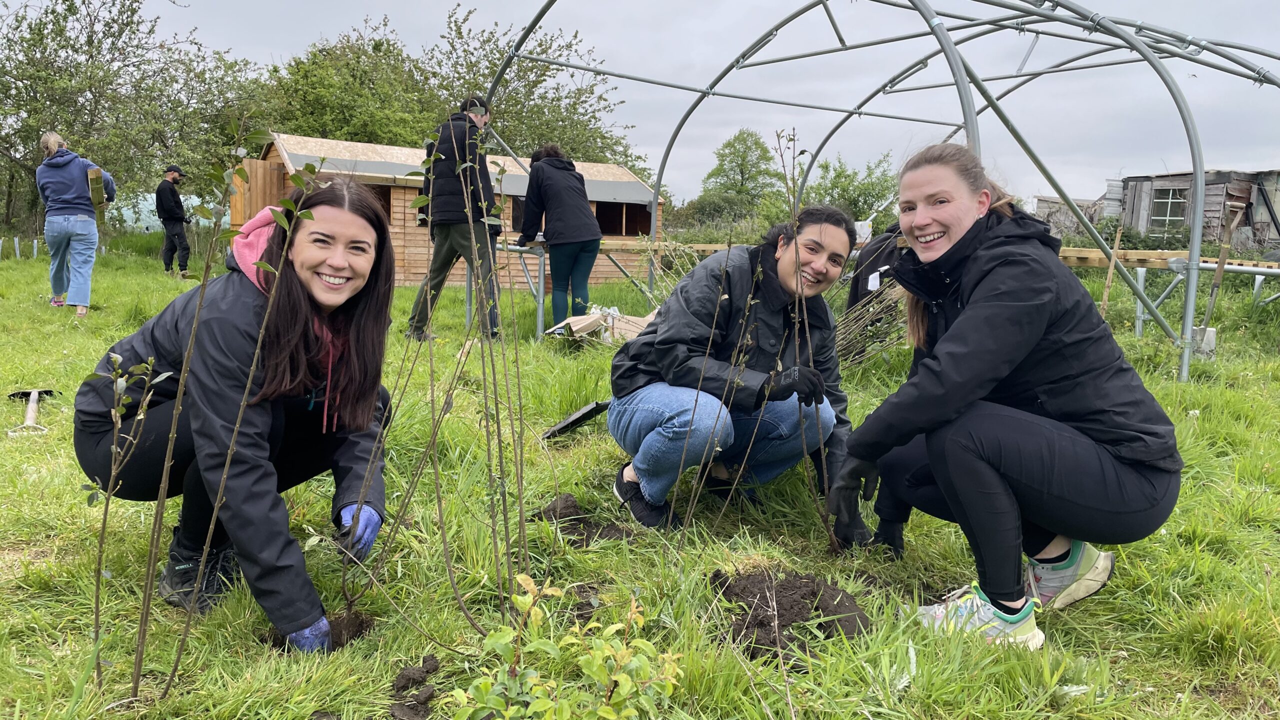 Three young women doing gardening in allotment space, smiling at the camera.