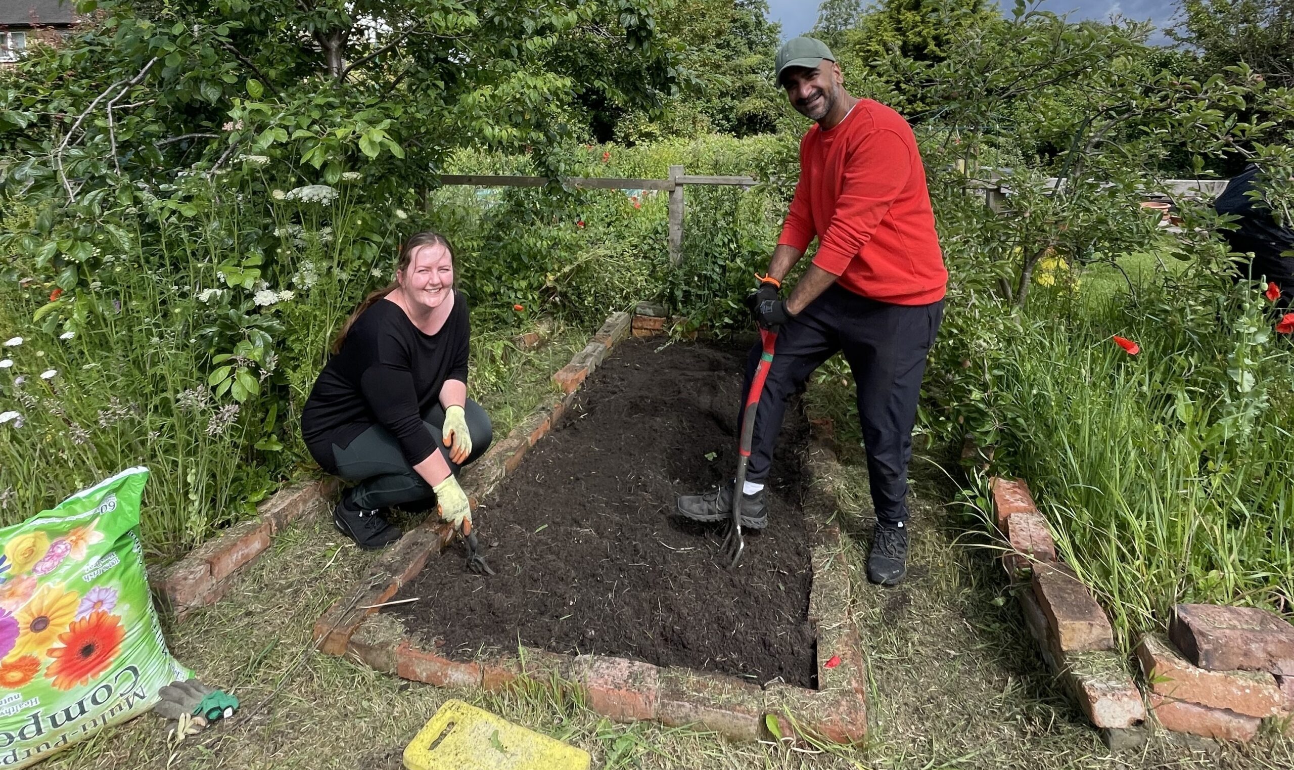 Man and woman working on raised bed in allotment space, smiling at the camera.