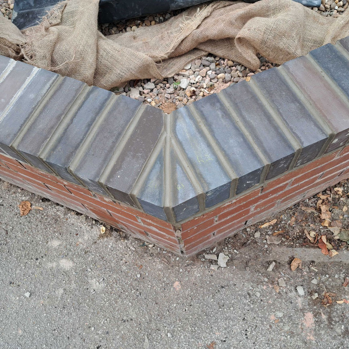 Low brick wall seen from above with blue brick on top and red brick at bottom, in outdoor environment