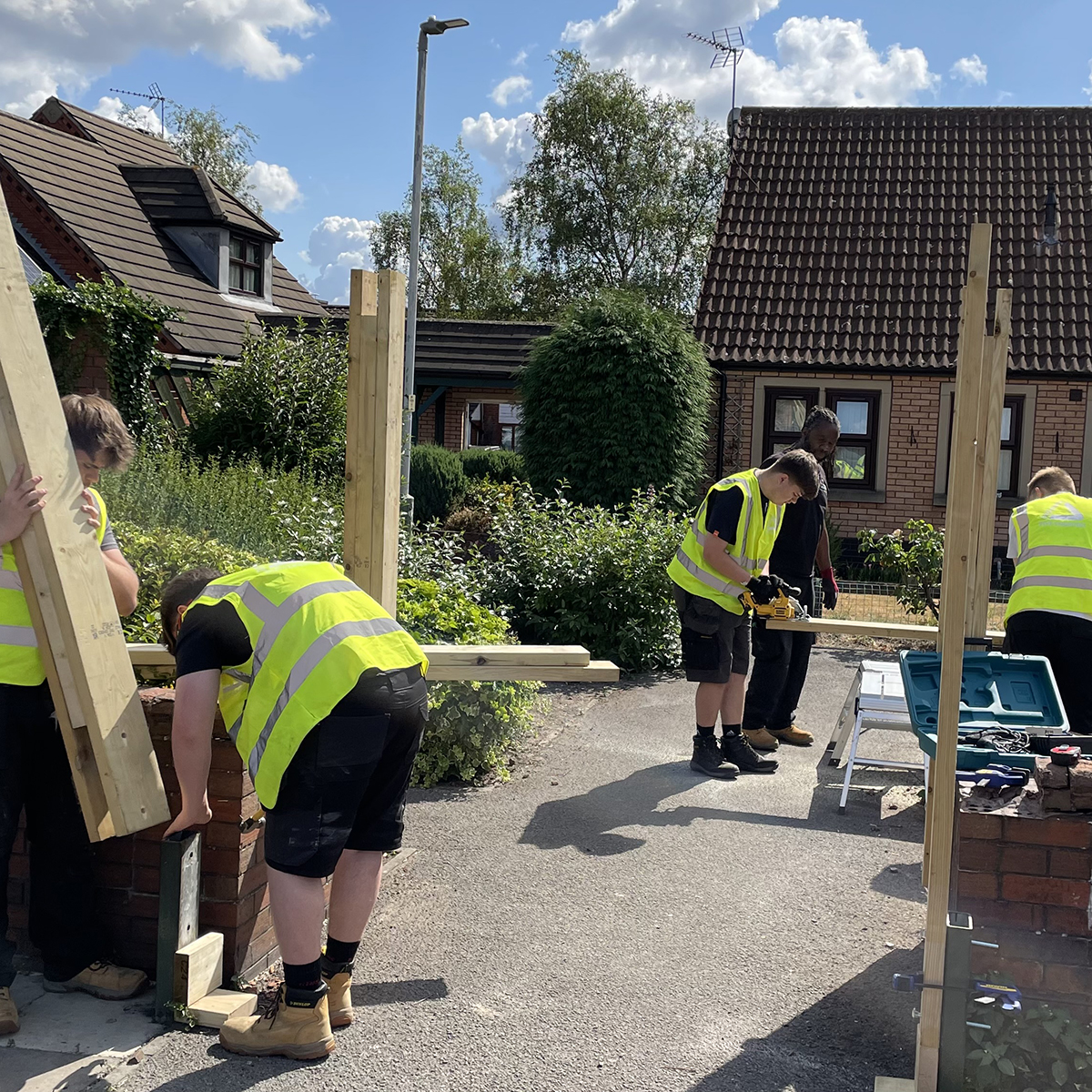 Young men wearing yellow high visibility vests working with wood in outdoor environment